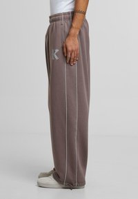Gray sweatpants with white side stripes, featuring an elastic waistband and an embroidered logo. Made of soft fabric with a relaxed fit.