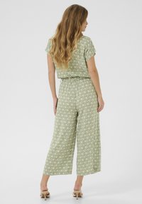 Combinaison à motif vert avec des manches courtes, taille élastique et design à jambes larges ; présente un imprimé de feuilles subtil sur un tissu léger.
