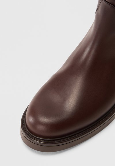 Botte en cuir brun avec une texture lisse, bout arrondi et une semelle en caoutchouc contrastante. Pas de motifs visibles ni de détails matériels.