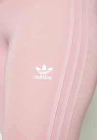 Ružičaste atletske tajice s glatkom teksturom, s tri bijele pruge sa strane i bijelim Adidas logom na bedrima.