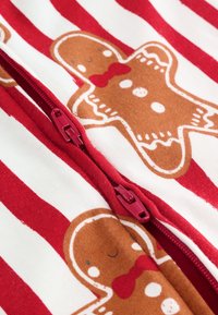 Czerwono-biała tkanina w paski z wzorem piernikowych ludzików. Przód zapinany na zamek błyskawiczny w dopasowanym czerwonym kolorze. Miękka bawełniana tekstura.