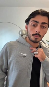 Camisola cinzenta com fecho éclair, feita de um material macio, com um logótipo branco da Nike e texto no lado esquerdo, com uma camisa preta por baixo.