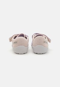 Zapatillas deportivas de malla de color rosa claro con suela de goma blanca, que cuentan con una correa y un sutil logo en el talón. Las zapatillas tienen un diseño transpirable.
