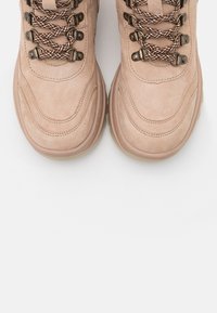 Scarpe da trekking in suede beige con finitura testurizzata, dotate di lacci a motivo marrone e bianco, occhielli metallici e una suola in gomma spessa.