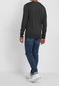Grå stickad tröja med rund halsringning och långa ärmar, ihop med blå denimjeans och vita hög-top sneakers.
