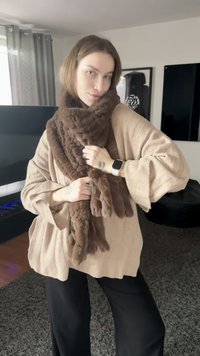 Brown faux fur scarf draped over light beige oversized sweater with textured fabric, featuring wide sleeves and a loose fit. Black pants.