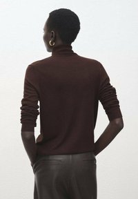 Pulover maro cu guler înalt, mâneci lungi, manșete reiate și croială ajustată, asortat cu pantaloni din piele întunecată. Textură fină.