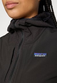 Close-up of a person wearing a black Patagonia jacket with a zipper and visible brand logo on the chest.