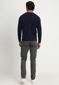 Marineblauer Pullover mit V-Ausschnitt, gerippten Bündchen und Saum, kombiniert mit grauen Slim-Fit-Hosen und weißen Sneakers. Minimalistischer und monochromatischer Look.