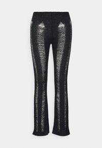 Svarta stickade byxor med vertikala slitna ränder som avslöjar huden under, med en åtsittande midja och utsvängda benöppningar.