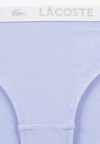 Light purple cotton underwear with a soft texture and a white waistband featuring the "LACOSTE" logo in gray. Simple design without patterns.