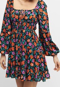 Robe florale avec un fond noir, des roses colorées orange et roses, des manches bouffantes, un décolleté carré et une taille froncée.