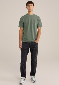 Zelena bombažna majica s kratkimi rokavi, okroglo izrezana, v kombinaciji s temno sivimi kavbojkami. Prijeten dizajn z sproščenim krojem in minimalnimi detajli.