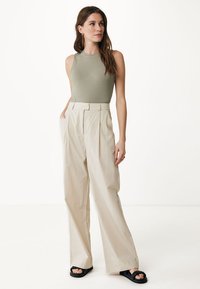 Hellbeige weite Hosen mit Falten, kombiniert mit einem taillierten olivgrünen Ripp-Top und schwarzen Slipper-Sandalen. Schlichtes, sauberes Design.