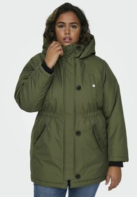 Olivgrön vadderad parka-jacka med huva, som har två sidofickor, knappstängning, elastisk midja och kontrasterande svarta mudd.