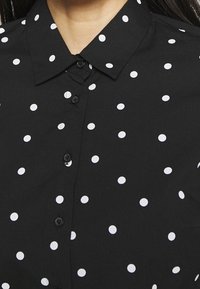 Czarna koszula z kołnierzykiem w białe kropki, z guzikami na przodzie i gładką teksturą materiału.