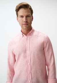 Hellrosa Button-Up-Hemd mit feinem Streifenmuster, langen Ärmeln und klassischem Kragen, aus einem strukturierten Stoff gefertigt.