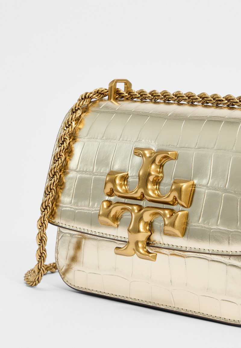 Metallisch goldene Handtasche mit krokodilprägung, ausgestattet mit einem markanten goldenen Logo und einem geflochtenen Kettenriemen. Strukturierte Form mit Klappenverschluss.