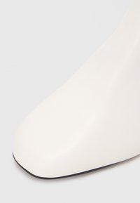 Bottine blanche à cheville avec un dessus en synthétique lisse, bout pointu et semelle noire. Le design est épuré avec un minimum de détails.