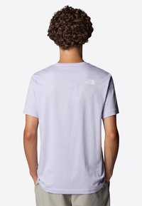 Jasnofioletowa koszulka z krótkim rękawem, wykonana z miękkiego materiału. Posiada małe białe logo na górnej części pleców. Klasyczny dekolt w kształcie łódki.