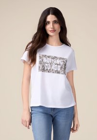 Tricou alb din bumbac, cu mâneci scurte și o croială lejera, având un patch din paiete argintii cu textul "NU AM NIMIC DE ADĂUGAT."