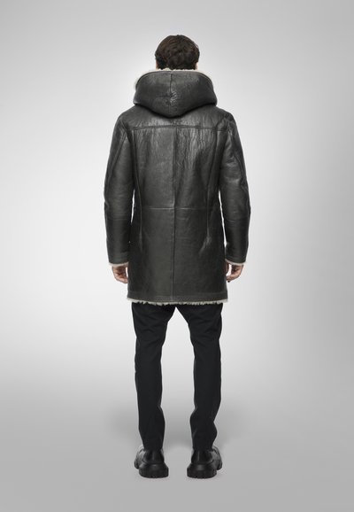 Cappotto di pelle nera con un ampio cappuccio, dettagli di texture sul materiale, rifinito con pelliccia lungo l'orlo. Indossato con pantaloni e scarpe neri.
