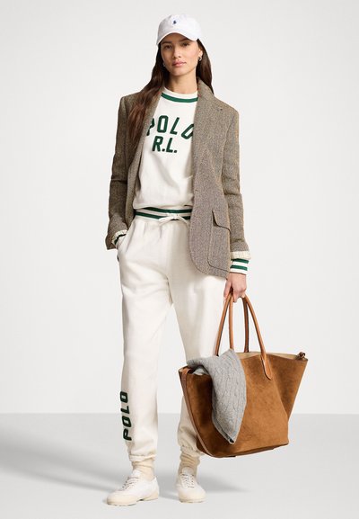 Blazer v károvanom vzore cez biely sveter s zeleným nápisom "POLO R.L.", krémové teplákové nohavice, biele tenisky a hnedá taška s šedým prikrývkou.