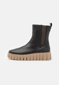 Bottine noire en cuir avec des panneaux élastiques sur les côtés, une finition texturée noire et une semelle en caoutchouc beige épaisse.