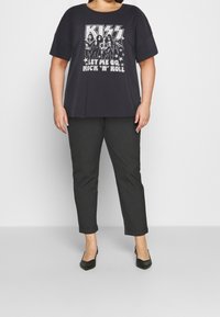 Sort grafisk t-shirt med KISS design og teksten "LAD MIG GÅ ROCK 'N' ROLL." Sammen med mørkegrå tapered bukser og sorte højhælede sko.