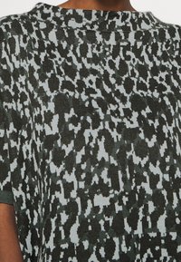 Pletený svetr s kulatým výstřihem, s abstraktním vzorem v černé a světle modré barvě na texturovaném povrchu. Krátké rukávy, volný střih.