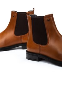 Botas Chelsea de cuero marrón con paneles laterales elásticos y una lengüeta. Presenta una punta redondeada y un tacón de goma bajo para mayor estabilidad.