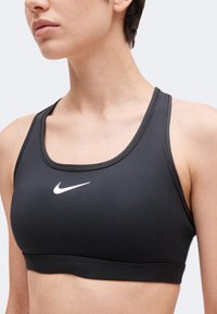 Close-up af en person, der bærer en sort Nike sports-bh med et hvidt Nike-logo på brystet.
