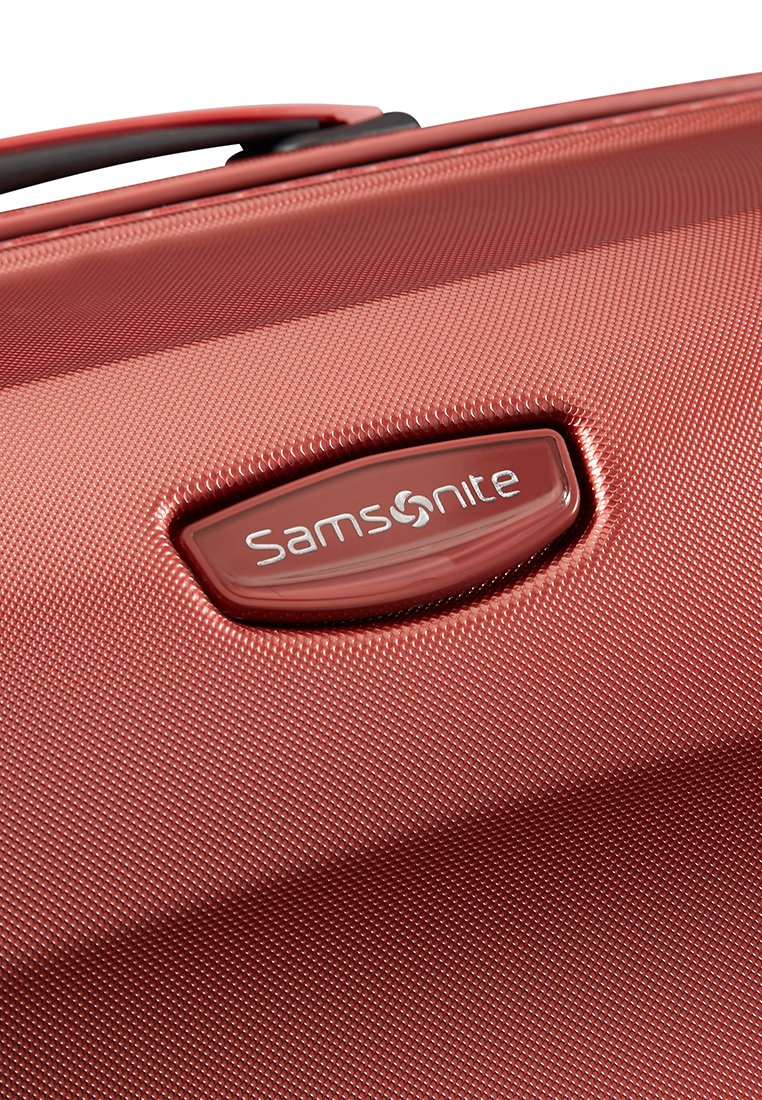 Maleta roja con una superficie texturizada, que presenta un logotipo plateado prominente y una forma aerodinámica para facilitar su manejo.