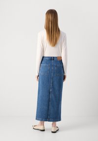 Falda maxi de mezclilla en azul, con corte recto, dos bolsillos traseros y un parche de cuero marrón en contraste en la cintura.
