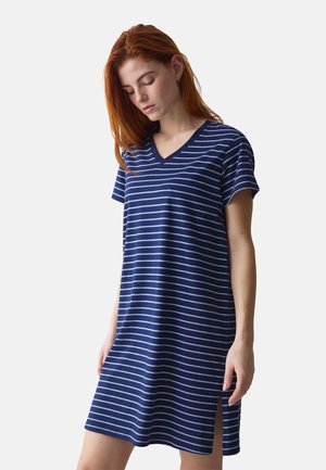 Junge Frau mit roten Haaren, die ein dunkelblau-weiß gestreiftes V-Ausschnitt-Kleid mit kurzen Ärmeln und seitlichem Schlitz trägt.