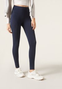 Marinblå leggings i stretchmaterial med hög midja. Bärs med vita sneakers som har nät- och solida detaljer.