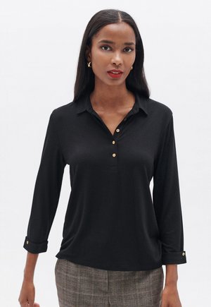Zwarte longsleeve polo met een kraag en drie gouden knopen bij de hals; lichte stof met opgerolde mouwen en een ontspannen pasvorm.