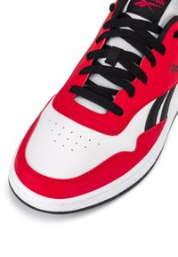 Piros és fehér sportcipő sima bőr felsőrésszel, fekete fűzőkkel, perforált orral és vastag gumi talppal.
