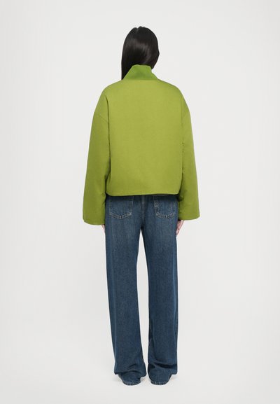 Short green cropped jacket with a high collar, paired with wide-leg blue jeans. The fabric looks textured and slightly padded.