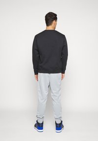 Svart sweatshirt och grå mjukbyxor, avslappnad passform. Sweatshirten har ribbad krage och mudd. Skorna är svarta med blå detaljer.