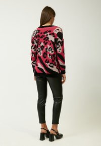 Gebreide trui met luipaardprint in roze en zwart, met lange mouwen, een ronde hals en ribbelranden, gecombineerd met zwarte leren broek.