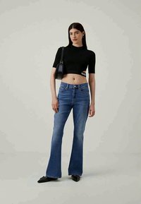 Black cropped top with short sleeves and a logo detail, paired with light blue flared jeans. Smooth fabric and a fitted design. Black handbag.