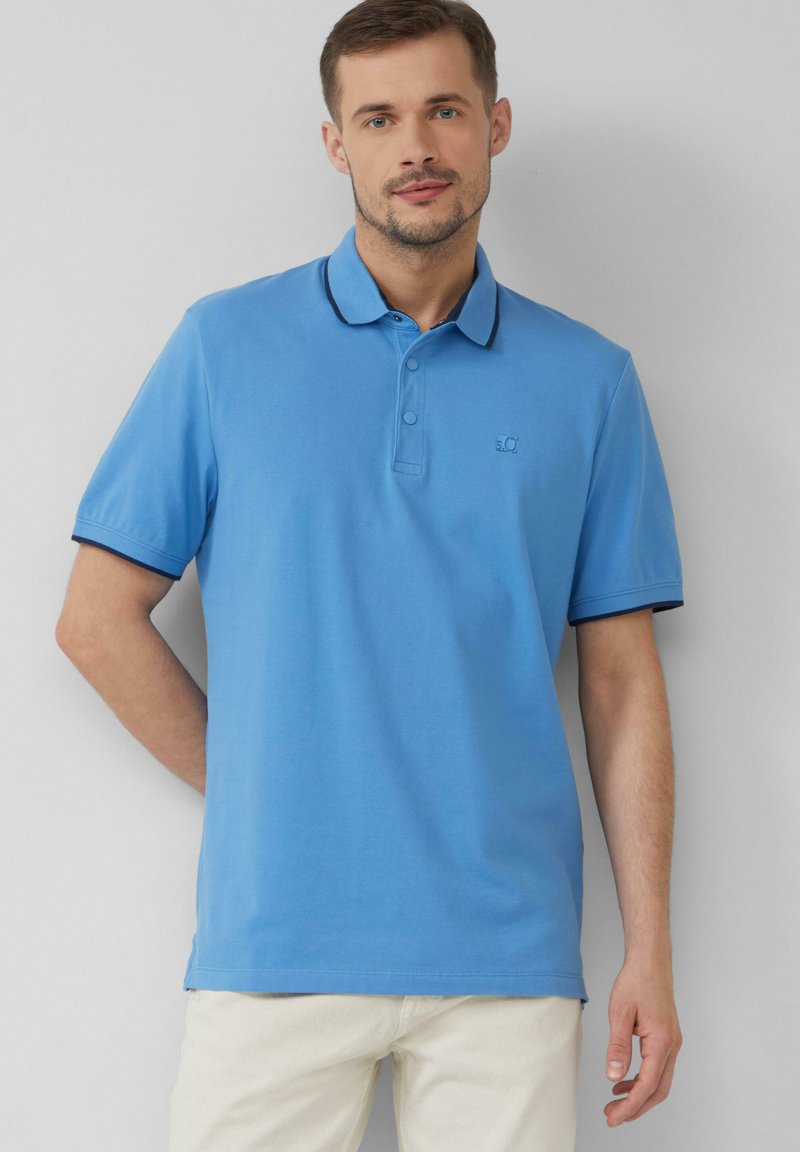 Lichtblauwe polo met korte mouwen, kraag en een knoopsluiting met twee knopen. Heeft een marineblauwe afwerking op de kraag en een klein logo op de borst.