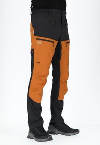 Vandringbyxor med en kombination av svart och orange färg, flera dragkedjefickor, en figurnära design och ett hållbart, flexibelt material.