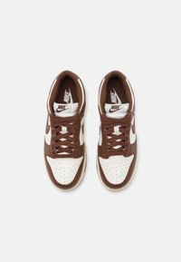 Paire de baskets Nike marron et blanches avec des lacets, vue de dessus sur un fond clair uni.