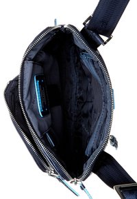 Borsa blu navy con chiusura a zip, abbinata a una tracolla con dettagli blu. L'interno presenta più scomparti e una fodera in tessuto liscio.