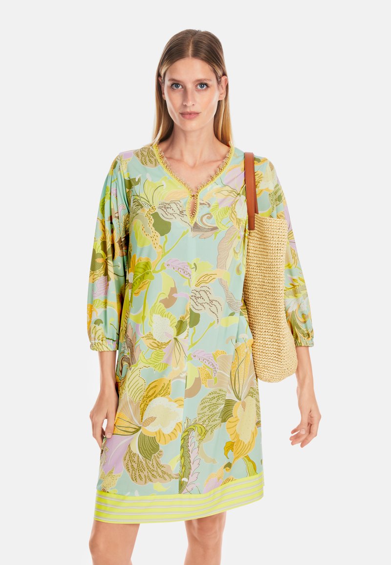 Kleid mit Blumenmuster in Hellblau, mit grünen, gelben und rosa Mustern. Auffälliger Schlitz-Halsausschnitt und kurze, elastische Ärmel.