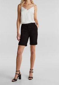 Musta muokattu lyhyt housut käännetyllä lahkeella, yhdistetty valkoiseen pitsireunukseen varustettuun toppiin ja mustiin hihna-korkkareihin.