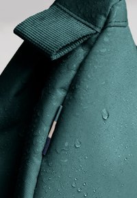 Tessuto teal con una finitura testurizzata, impreziosito da gocce d'acqua, colletto piegato e un dettaglio di rifinitura a contrasto in blu e beige chiaro.
