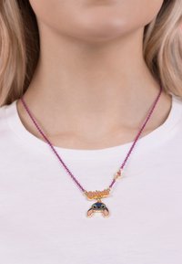 Collier en perles violettes avec un accent doré, portant le mot "Stitch !" et un charme de manette de jeu en cartoon bleu.
